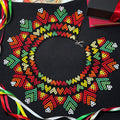 Colorful embroidered design on black fabric with ribbons and books in the background